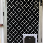 White Dogwalk wood-fitting Medium dog door installed in a metal mesh security door