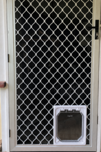 Dogwalk medium dog door in white fitted into a metal mesh security door