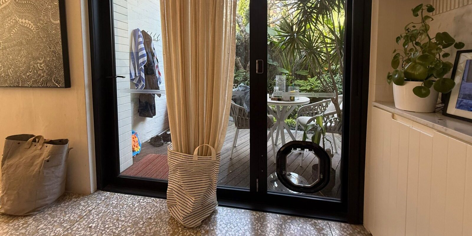 Black Dogwalk dog door fitted low in the glass of a black-framed aluminium door, opening onto a deck and garden