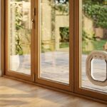 White Dogwalk Intermediate Slim Line dog door in a timber-framed bi-fold glass door, with a dog on the patio outside